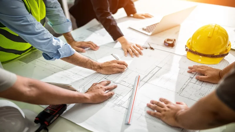 Une équipe de professionnels examine des plans de construction sur une table, symbolisant la planification et la collaboration dans les projets de rénovation.