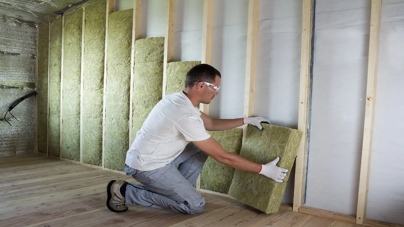 Un ouvrier installant des panneaux d'isolation thermique en laine de roche sur une ossature en bois, dans le cadre de travaux de rénovation intérieure.