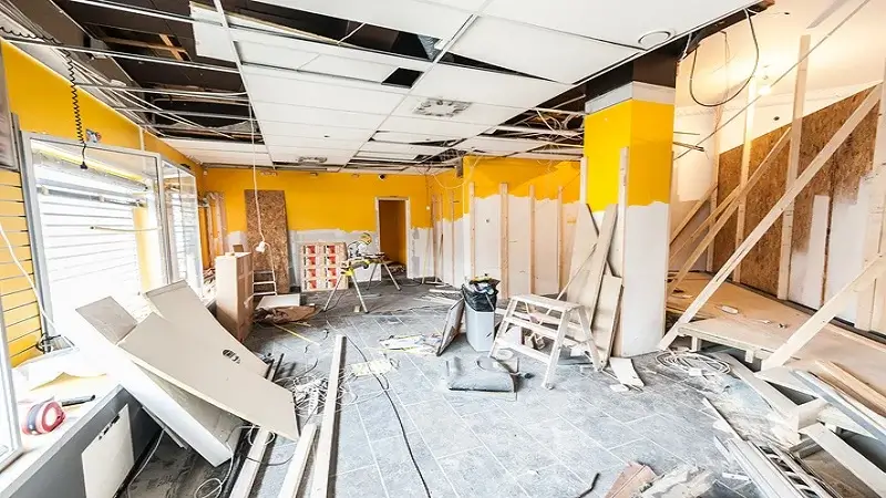 Un espace en pleine rénovation avec des murs en cours de préparation, un plafond partiellement démonté, et des matériaux dispersés, illustrant les étapes structurantes d’un chantier de transformation intérieure.