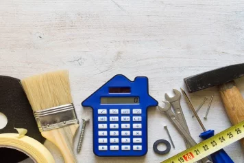 Le coût de rénovation d’une maison, avec une calculatrice en forme de maison entourée d’outils de bricolage, symbolisant l’estimation budgétaire et la planification des travaux.