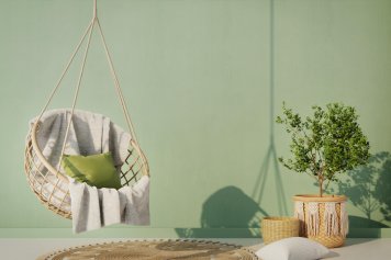 Vue sur un coin lecture au style de décoration intérieure zen et nature, avec u fauteuil suspendu sur un tapis de juste et quelques plantes dans le coin de l'espace.