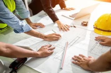 Une équipe de professionnels examine des plans de construction sur une table, symbolisant la planification et la collaboration dans les projets de rénovation.