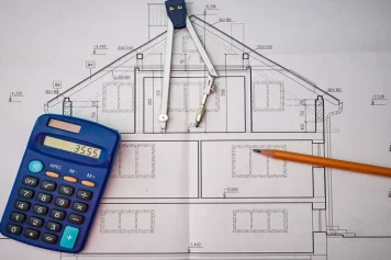 La planification d’une rénovation de maison, avec un plan architectural détaillé, une calculatrice, un compas et un crayon, symbolisant le calcul des coûts, la conception des travaux et l’élaboration du budget de rénovation.