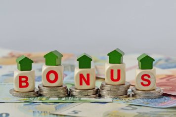 La photo représente des dés avec les lettres BONUS et des petites maisons dessus, posés sur des pièces de monnaies pour représenter la rénovation maison aide financière.