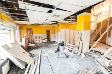 Un espace en pleine rénovation avec des murs en cours de préparation, un plafond partiellement démonté, et des matériaux dispersés, illustrant les étapes structurantes d’un chantier de transformation intérieure.